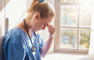 Bildet viser en sykepleier med fremoverbøyd hode. Hun er sliten og kniper seg over neseryggen