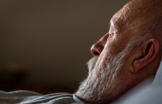 Bildet viser en eldre mann i profil med lukkede øyne. Han ligger i sengen.
