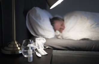 Bilde av person til sengs med forkjølelsesmidler på nattbordet