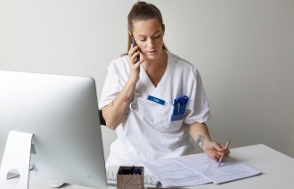 Bildet viser en ung, kvinnelig sykepleier som snakker i telefonen og tar notater.