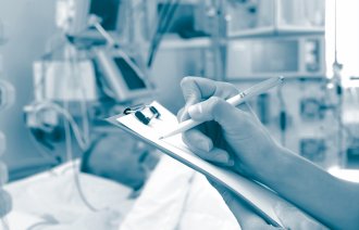 Bildet viser en syk pasient på en intensivavdeling. I forgrunnen ses et skjema og hendene til en sykepleier som skriver på skjemaet