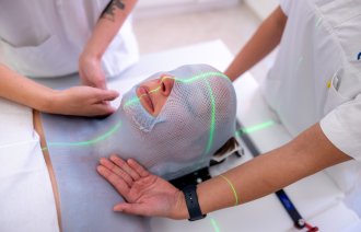 Bildet viser en pasient som skal få strpleterapi mot hodet. Vedkommende har en nettmaske på seg, og lysstriper viser hvor det skal stråles