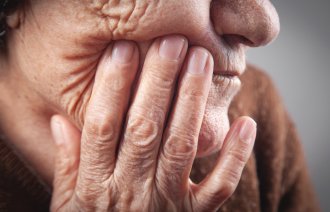 Munnhelse Bildet viser en eldre kvinne som tar seg til ansiktet ved munnen