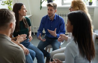 Bildet viser en gruppe mennesker som sitter i ring og snakker sammen