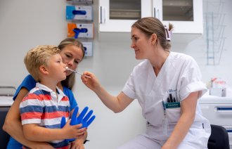 Bildet viser en liten gutt på fanget til sin mor. En sykepleier gir ham nesespray inn i det ene neseboret