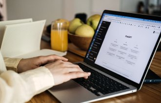 Bildet viser et par hender som skriver på et pc-tastatur. På pc-skjermen står det ChatGPT.