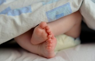Bildet viser to små barneføtter som stikker ut av en dyne.