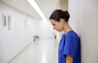 Bildet viser en sykepleier med bøyd hode som lener seg til en vegg. Hun er trist.