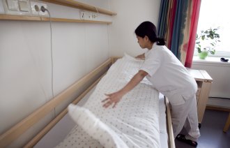 Bildet viser en helsefagarbeider som rer opp en seng.