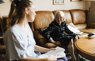 Bildet viser en sykepleier i hjemmetjenesten som snakker med en eldre pasient