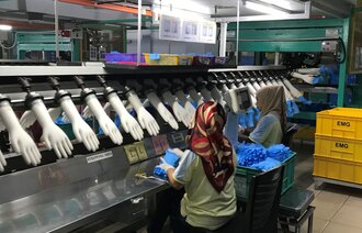 Bildet viser arbeidere på en hanskefabrikk i Malaysia.