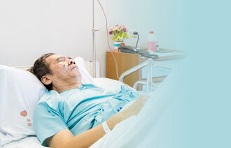 The photo shows a sick man lying in a hospital bed. On the bedside table there are flowers and a bottle. On the pillow there are some drops of blood