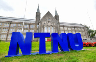 Bildeviser logoen til NTNU på gressplenen foran den gamle hovedinngangen 