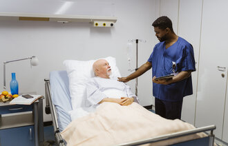 Bildet viser en sykepleier som står ved sengen til en pasient