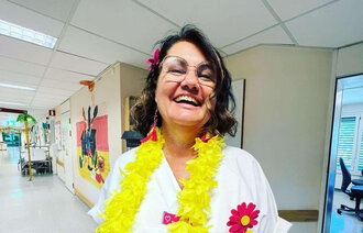 Sykepleier på jobb. hun har blomster rundt halsen og smiler.