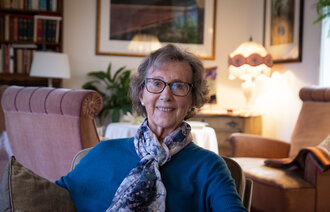 Signy Romslo sitter hjemme i soffa og siler til kamera