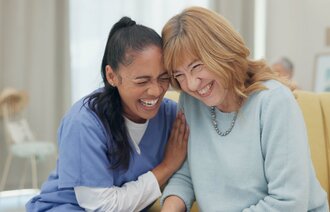 Bildet viser en ansatt og en beboer på sykehjem som ler sammen.