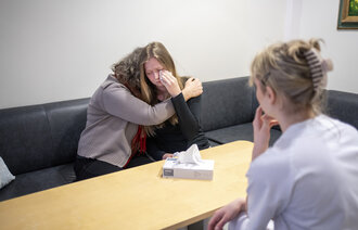 Bildet viser en ung, gråtende pasient som får en klem av pårørende. Bildet viser også en sykepleier som sitter på motsatt side av bordet.