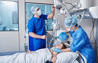 Bildet viser to intensivsykepleiere ved sengen til en pasient som ventileres.