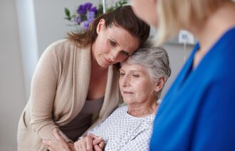 Bildet viser en alvorlig syk kvinne med en sykepleier og familie rundt seg