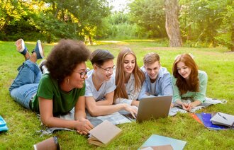 Bildet viser en gjeng studenter som jobber sammen på en laptop utendørs