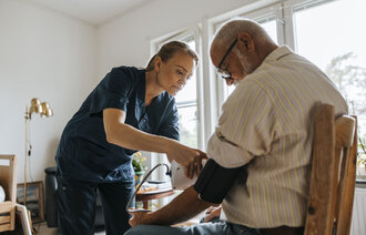 Bildet viser en sykepleier som måler blodtrykket på en eldre pasient i hjemmet