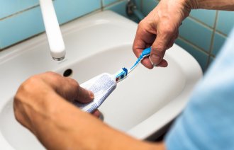 Bildet viser to hender som tar tannkrem på en tannbørste.