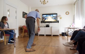 Bildet viser en eldre mann som spiller bowling på storskjerm ved hjelp av Kinect.