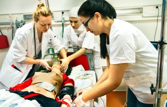 Sykepleier- og legestudenter øver på en akuttsituasjon med en dukke i sykesengen.