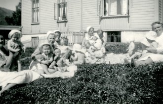 Historisk, gammelt bilde av sykepleiere med små barn på gresset utenfor Bergen kommunale mødrehjem.