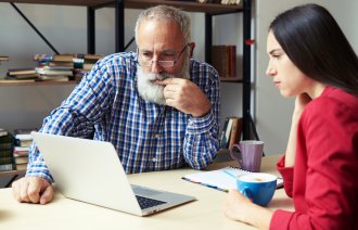 Ung jente viser en eldre mann noe på PC-en sin på et kontor