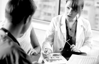 Bildet viser ei dame i hvit frakk som viser to personer et ark med et diagram på.