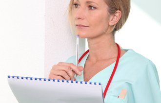 En kvinnelig sykepleier står og tenker med en penn og skriveblokk