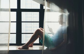 Ung mann sitter med mobil bak gardin.