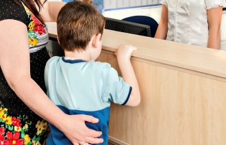 Bildet viser en mor og et barn som står foran en skranke med en kvinne bak