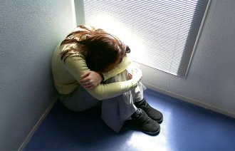 Bildet viser en jente som sitter på gulvet med hodet skjult mellom bena