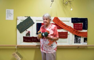 Bildet viser demenssyke Ragnhild på Fosshagen dagsenter i Lier. Hun står foran en tavle med lapper hun har strikket. På lappene står blant annet "alene", "savn" og "ærlig".