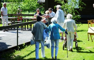 Eldre personer som går over en gressplen på vei til et arrangement. Noen har rullator.