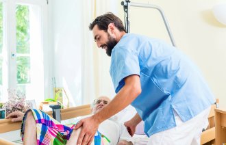 Bildet viser en eldre mann som blir stelt av en mannlig sykepleier.