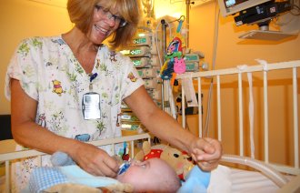 Bildet viser Britt Elin Fredriksen som kommuniserer med en liten baby som ligger i en sykehusseng.