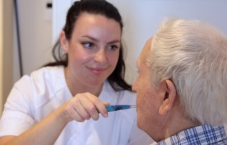 Sykepleier utfører munnstell på en eldre mann Bildet viser en sykepleier som pusser tennene til en eldre mann