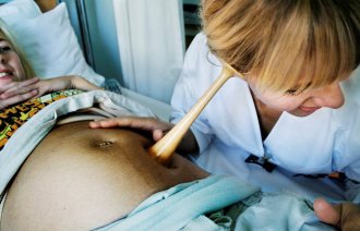 Bildet viser en jordmor som lytter på en mage med jordmorstetoskop.