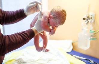 Bildet viser en nyfødt baby som løftes opp kort tid etter fødselen