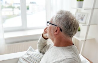 Lyst kledd middelaldrende mann sitter og ser ut av vindu. Hvitt lys.