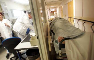 Bildet viser korridorpasient på sykehus. Helsepersonell jobber i bakgrunnen