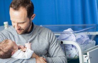 Bildet viser en nybakt far som holder en nyfødt baby