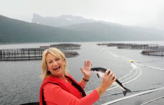 Torill er ute ved et fiskeoppdrettsanlegg. Hun holder en fisk i hånden.