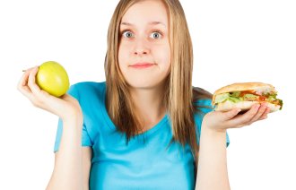 En jente holder en hamburger i ene hånden og ett eple i den andre. Valgets kval