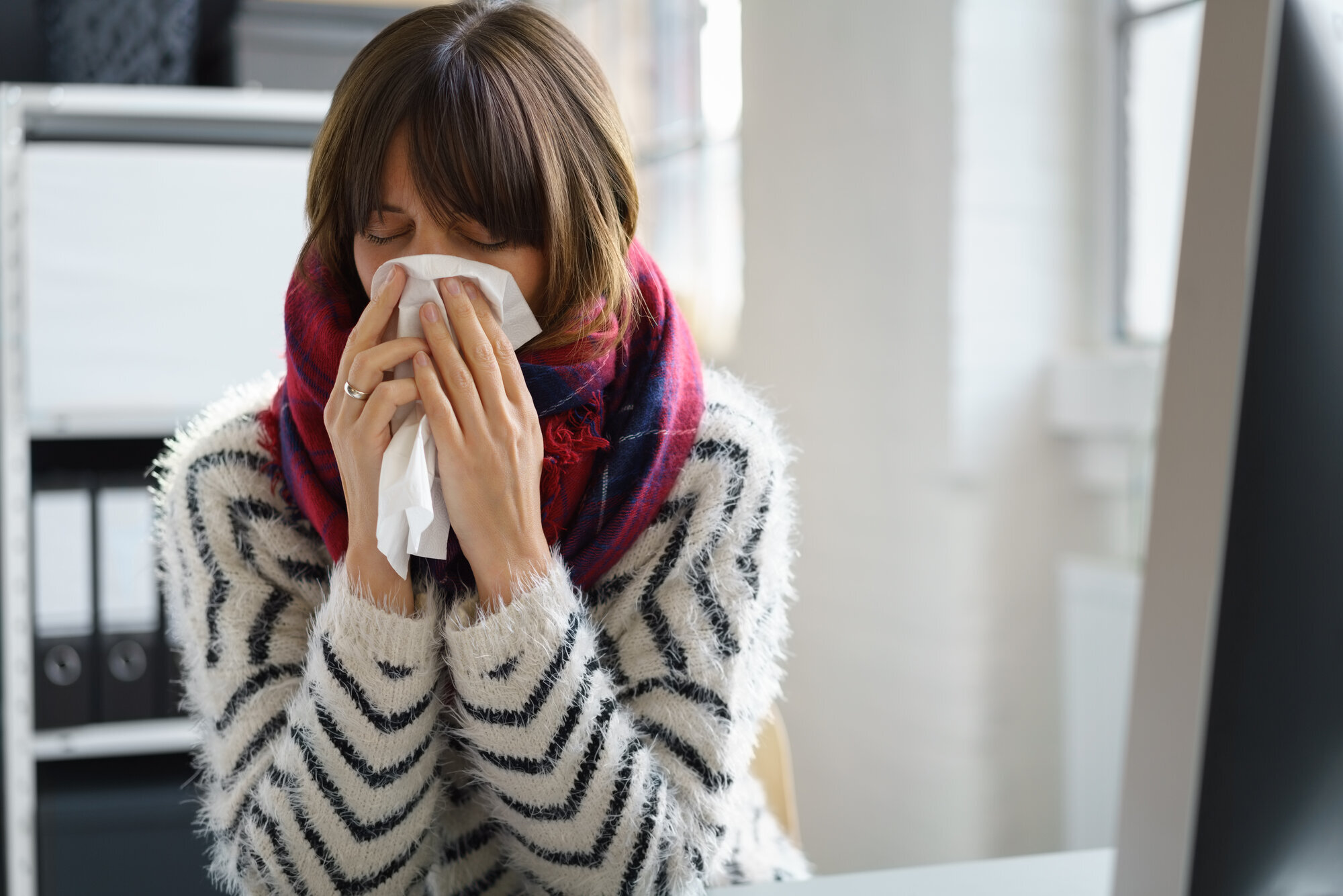 Kvinne med myk strikkegenser og mørkt glatt hår gjemmer ansiktet i et lommetørkle.