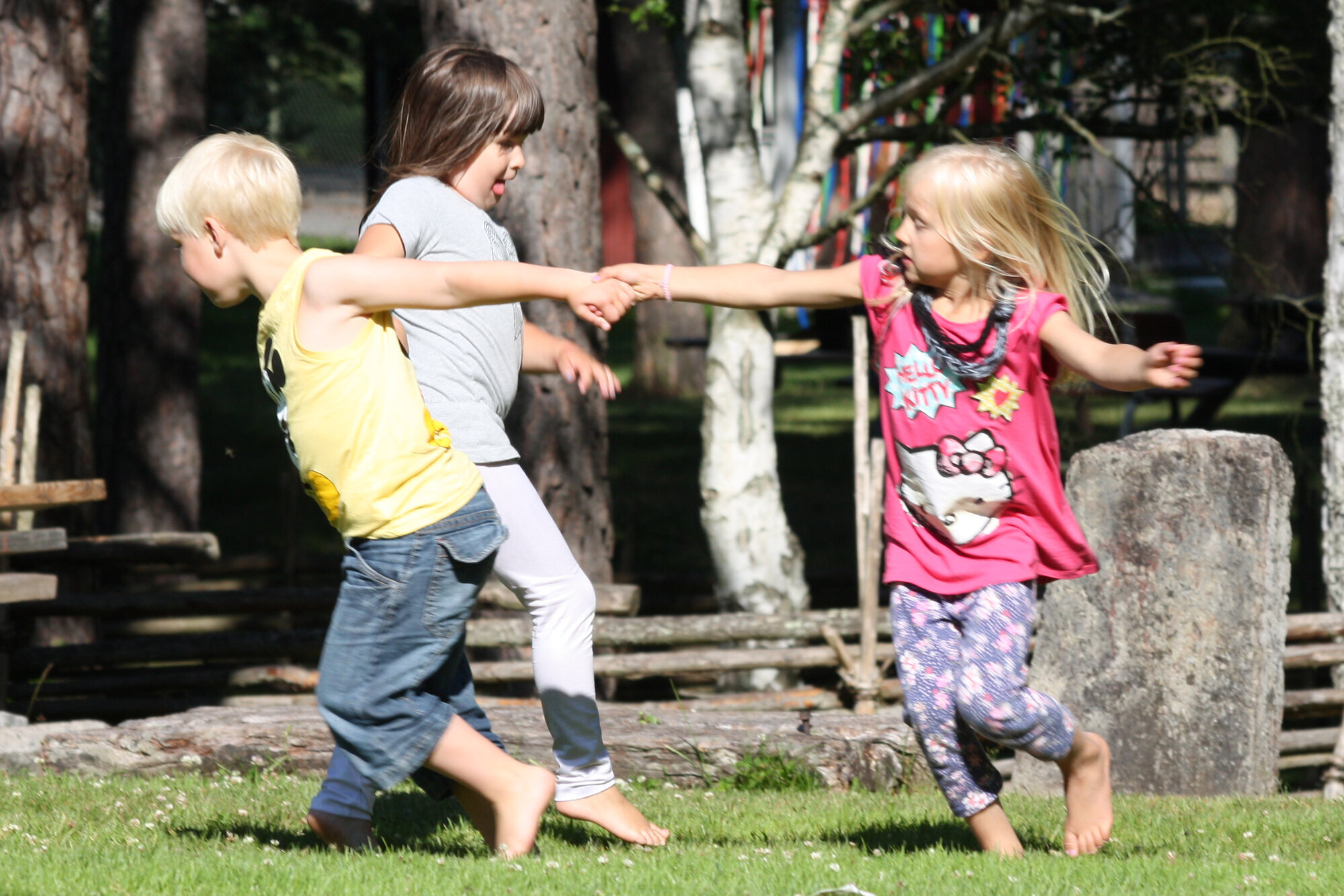 Tre nordisk utseende barn leker i ring. Lettkledde i sommervær.
